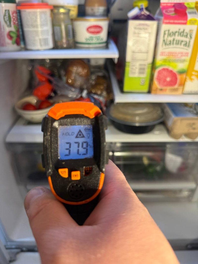 Infrared thermometer reading 37.9°F on a refrigerator shelf after the repair