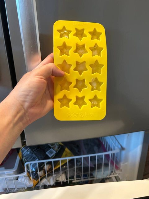 Silicone star ice tray held in front of an open freezer drawer while the ice maker is tested