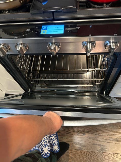 Gas range with the oven door open and the touch display lit during an igniter and temperature check